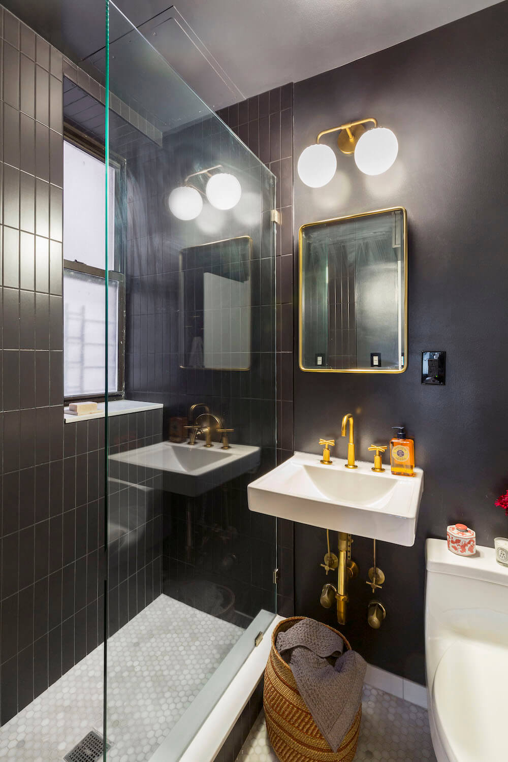 shower-with-black-subway-tiles bathroom with floating sink and gold faucet and fixtures and black paint on wall and walk-in shower with black subway tiles and glass wall after renovation