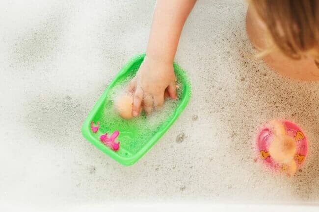 little baby girl playing with foam in a bath tub. girl takes a bath with a doll.